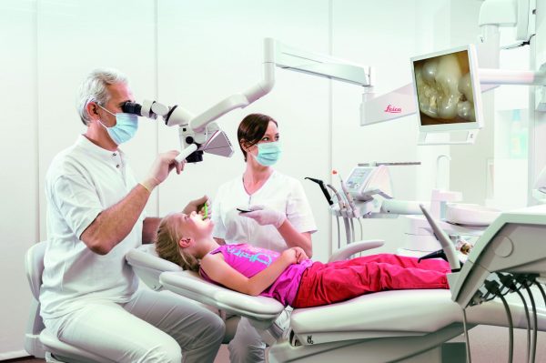 Tandlæge og klinikassistent bruger Leicas M320 High End dentalmikroskop på barnepatient